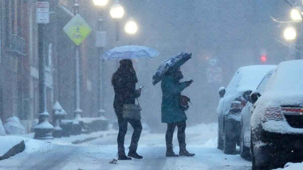 Người dân che ô để tránh tuyết rơi khi họ đi qua một con đường ở khu phố North End Boston ngày 15/3 - Nguồn: AP