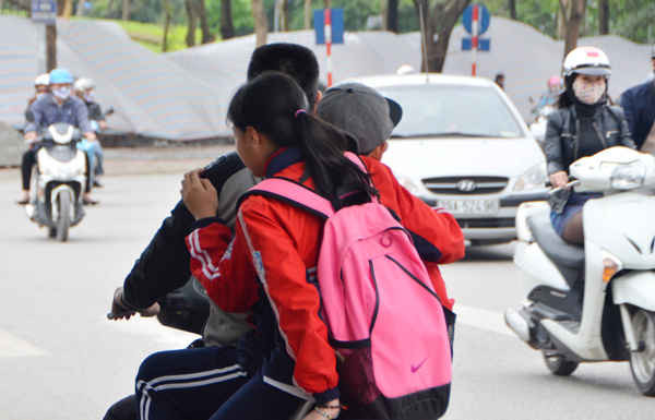 Ba người ngồi trên xe máy không ai có mũ bảo hiểm khi tham gia giao thông, phụ huynh nào cũng thế này thì sao bảo được các em học sinh.