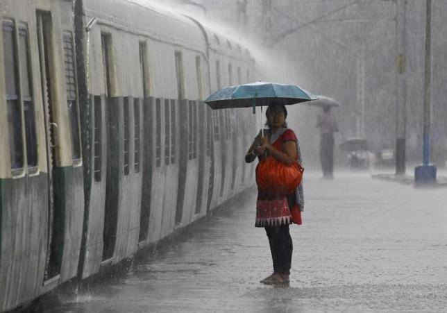  Một người phụ nữ đứng che ô và chờ chuyến tàu trong một trận mưa lớn tại nhà ga ở Kolkata ngày 20/9/2014. Ảnh: REUTERS / RUPAK DE CHOWDHURI
