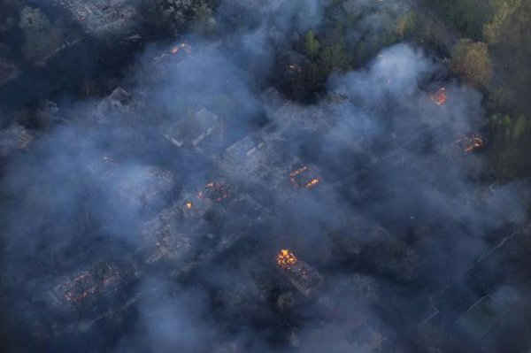 Nhìn từ trên không qua cửa sổ của một máy bay trực thăng, thấy được lửa cháy và khói bốc lên từ các tòa nhà của một làng bị bỏ hoang ở miền bắc Ukraina ngày 28/4. Ảnh: REUTERS / ANDREW Kravchenko / POOL