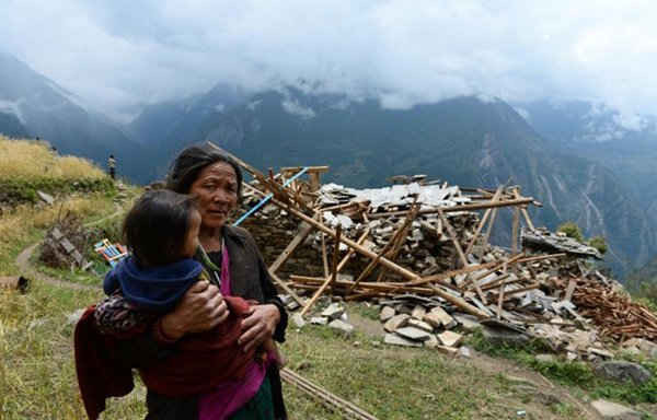   Một người mẹ bế đứa con đi ngang qua một ngôi nhà bị phá hủy tại làng Uiya, huyện Gorkha vào ngày 29/4. Ảnh: Sajjad Hussain / AFP