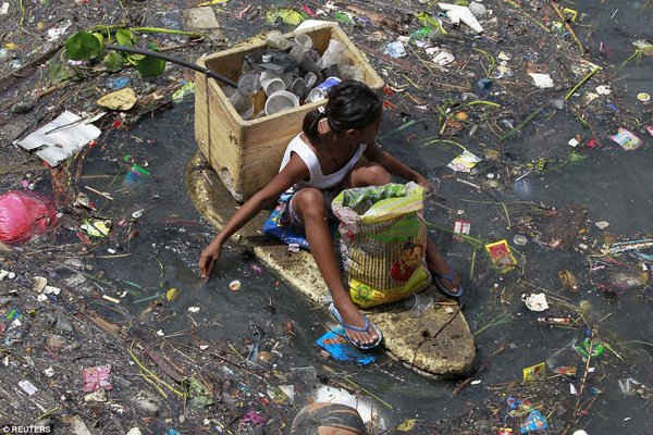 Một cô bé ngồi trên chiếc bè xốp để thu gom vật liệu tái chế trên dòng sông ô nhiễm nặng ở thành phố Navotas, phía bắc Manila