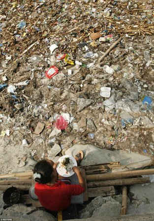 Một phụ nư vô gia cư ngồi ăn cơm trước bãi rác thuộc vịnh Manila