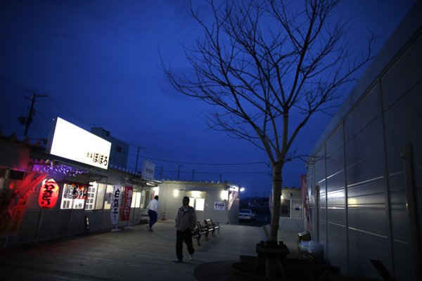 Người dân đi bộ dọc theo một trung tâm mua sắm được xây dựng tạm trong một khu vực bị ảnh hưởng bởi thảm họa động đất và sóng thần xảy ra ở Ofunato,tỉnh Iwate vào ngày 11/3/2011. Ảnh: Reuters