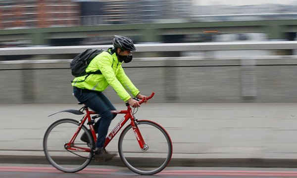 Một người đi xe đạp đeo khẩu trang qua Cầu London (London Bridge). Ảnh: Sang Tan / AP