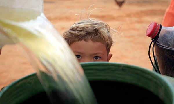 Cậu bé người Brazil xem mẹ đổ nước vào trong thùng. Ảnh: Ricardo Moraes / Reuters