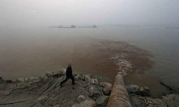 Người con trai đi qua một ống dẫn nước thải xả vô sông Dương Tử từ là một xí nghiệp sản xuất giấy tờ ở An Khánh, tỉnh An Huy, Trung Quốc. Ảnh: William Hồng / Reuters