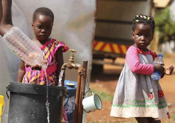 2 đứa trẻ ở Zimbabwe đứng xem mẹ lấy nước từ vòi nước công cộng ở Harare vào ngày 5/2/ 2016. Ảnh: REUTERS/PHILIMON BULAWAYO