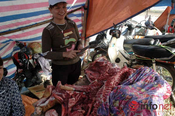 Một người phụ nữ cười vui vẻ, mài dao bán thịt bò ở lối vào chợ Viềng