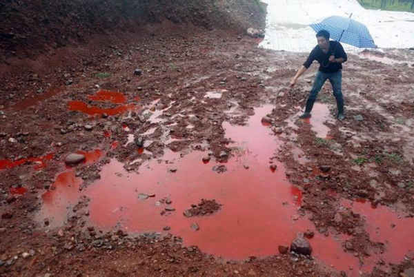 Người đàn ông chỉ vào đất và nước chuyển sang màu đỏ sau khi bị ô nhiễm bởi chất thải công nghiệp từ các nhà máy sản xuất thuốc nhuộm khép kín, giữa lúc mưa lớn tại một ngọn núi ở quận Ruyang, tỉnh Hà Nam ngày 15/9/2014. Ảnh: REUTERS / STRINGER