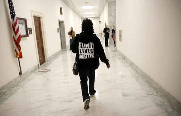Một phụ nữ mặc áo với dòng chữ sau lưng có ghi '' Flint Lives Matter'' (tạm dịch: Xem trọng sinh mạng của Flint) đi về phía phòng điều trần tại Capitol Hill, Washington vào ngày 17/3/2016. Ảnh: Reuters / Kevin Lamarque