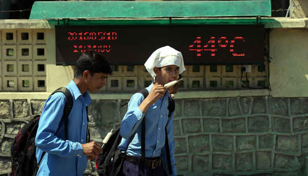 Những học sinh ăn kem khi đi bộ qua một màn hình ghi lại nhiệt độ 44 độ C ở Jammu, Kashmir. Ảnh: Jaipal Singh / EPA