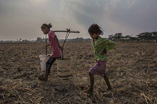 Ma Moe Thu, 11 tuổi và Zin Mar Win, 7 tuổi gánh nước sạch qua cánh đồng lúa về nhà của họ ở Dala, Myanmar. Sau khi gần như tất cả các hồ và ao nước ở Dala cạn khô, cư dân nơi đây hiện đang có nước uống từ các nhà tài trợ địa phương do các nhà sư Phật giáo tổ chức. Những nông dân ở Myanmar bị thiếu nước khi El Nino tạo ra nhiệt độ cao kỷ lục và gây hạn hán. Ảnh: Lauren DeCicca / Getty Images
