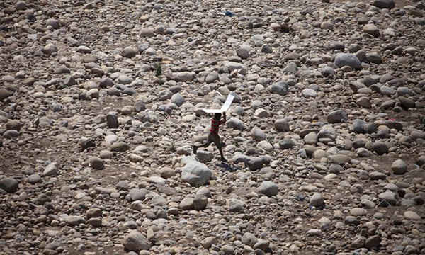 Một cậu bé bảo vệ mình khỏi ánh nắng mặt trời khi đi bộ trên lòng sông cạn nước ở Jammu, Ấn Độ. Đất nước này đã trải qua nhiệt độ nóng kỷ lục trong tháng 5/2016. Ảnh: Channi Anand / AP