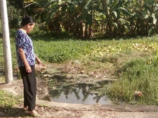 Bà Lê Thị Phinh bức xúc chỉ xuống ao nước thải đang khiến cuộc sống của gia đình cụ và người dân nơi đây bị đảo lộn vì mùi hôi thối