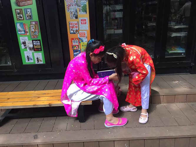 Hai chị em bé gái mặc áo dài truyền thống say sưa đọc một cuốn sách yêu thích