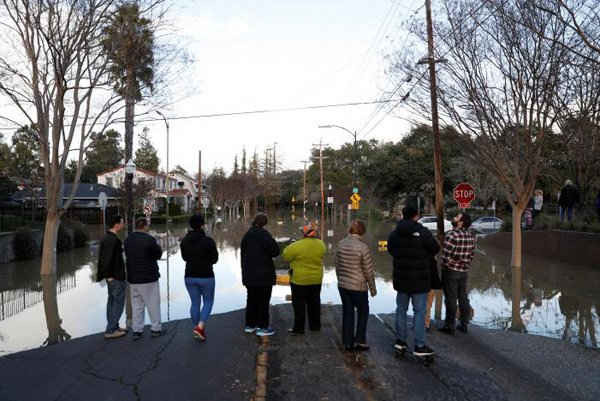 Người dân đứng trên một con phố bị ngập lụt gần William Street Park sau khi mưa lớn làm ngập con lạch Coyote ở San Jose, California, Mỹ vào ngày 21/2/2017. Ảnh: REUTERS / Stephen Lam