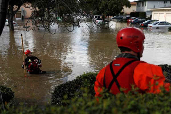 Một lính cứu hỏa cùng với Sở Cứu Hỏa San Jose lội trong một khu phố bị ngập lụt sau khi những trận mưa lớn tràn ngập con lạch Coyote ở San Jose, California, Mỹ. REUTERS / Stephen Lam