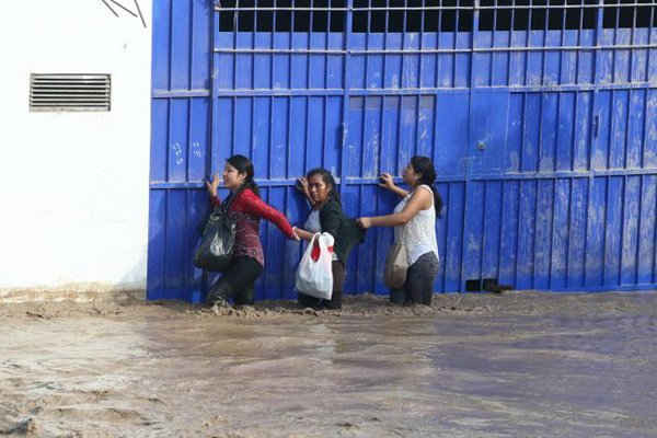 Những người phụ nữ dắt tay nhau đi qua một con đường bị ngập nước sau khi dòng sông Huayco tràn bờ khiến nước chảy qua các đường phố ở Huachipa, Peru vào ngày 17/3/2017. Ảnh: REUTERS / Guadalupe Pardo