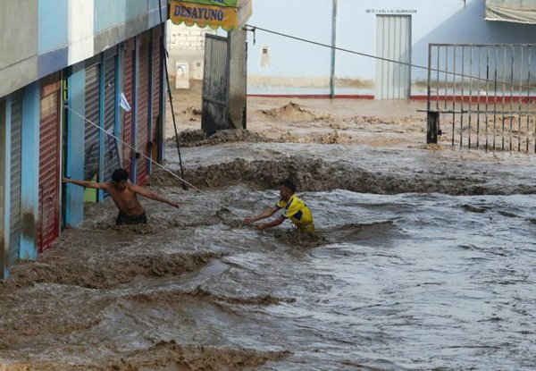 Một người đang cố gắng giúp hàng xóm của mình vượt qua con đường bị ngập nước sau khi dòng sông Huayco tràn bờ khiến nước chảy qua các đường phố ở Huachipa, Peru vào ngày 17/3/2017. Ảnh: REUTERS / Guadalupe Pardo