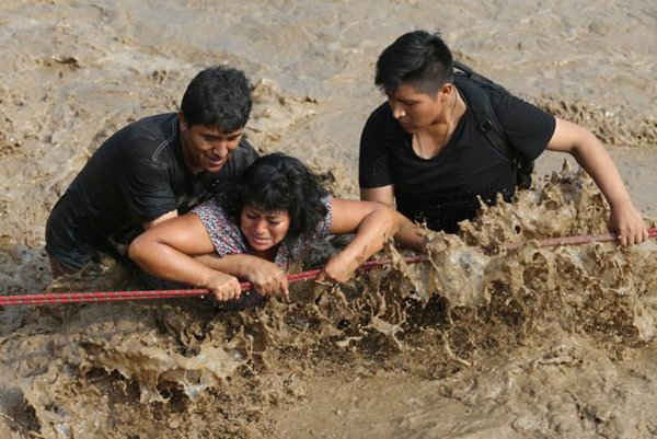 Mọi người vượt qua con đường bị ngập lụt sau vụ lở đất và lũ lụt lớn ở quận Huachipa thuộc Lima, Peru. Ảnh: REUTERS / Guadalupe Pard