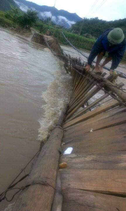 Người dân bản Nà Phát cố gắng vượt qua cây cầu treo bị lật do lũ suối rất nguy hiểm.