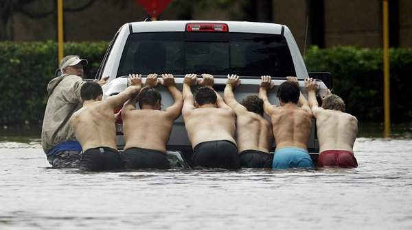 Nhiều người ra sức đẩy một chiếc xe bán tải bị mắc kẹt trong con đường ngập nước ở Houston. Ảnh: Charlie Riedel / AP