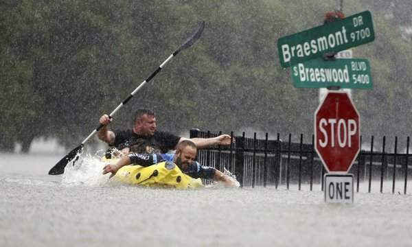 Hai người chèo xuồng cố gắng vượt qua dòng nước ngập lụt do lũ. Ảnh: Mark Mulligan / AP