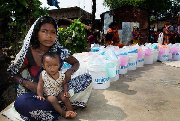Người phụ nữ và con của cô chờ đợi để nhận các vật phẩm cứu trợ do UNICEF phân phối, bao gồm màn chống muỗi và chăn.