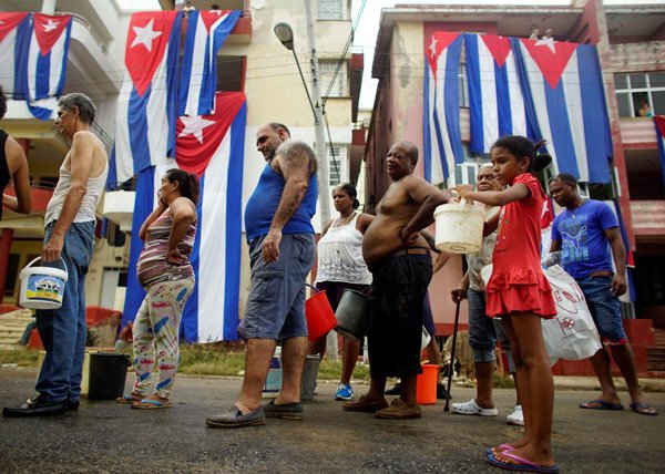 Người dân xếp hàng lấy nước uống từ một chiếc tàu chở nước của chính phủ bên cạnh các lá cờ Cuba đang được treo để phơi khô sau khi siêu bão Irma gây ngập lụt và mất điện ở Havana, Cuba ngày 11/9/2017. Ảnh: REUTERS / Alexandre Meneghini