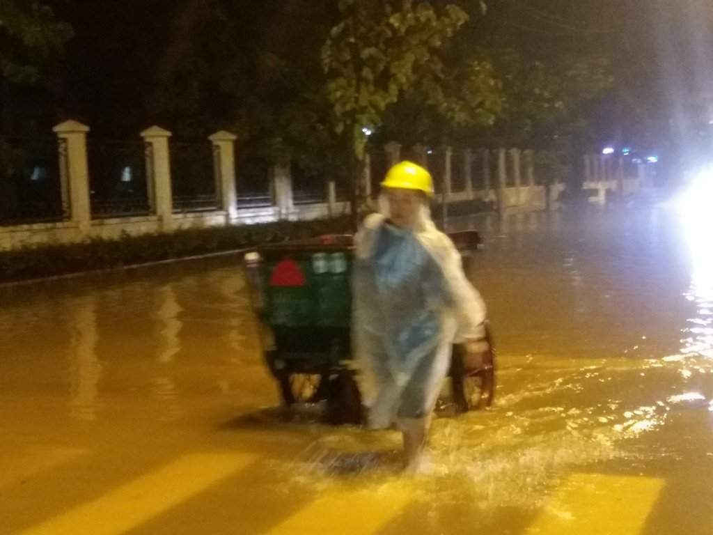 Một nữ công nhân đẩy xe rác trên tuyến đường còn ngập nước tại Trung tâm hành chính Tp Huế