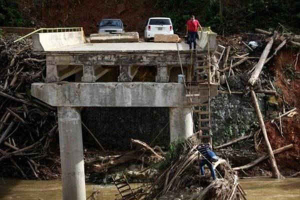 Một người phụ nữ giữ thang cho chồng của cô leo xuống tại một cây cầu bị phá hủy sau khi bão Maria đổ bộ Utuado, Puerto Rico hồi tháng 9. Ảnh: Alvin Baez