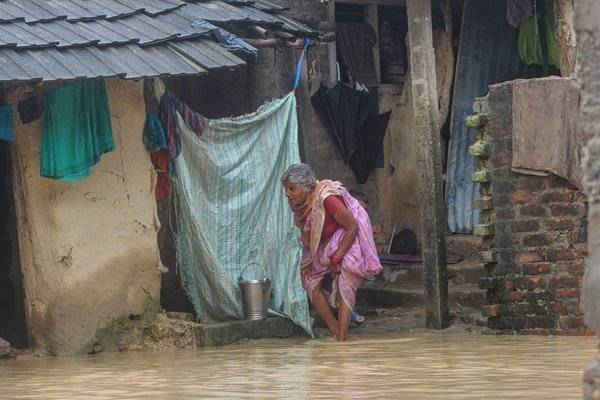 Một cụ bà đi bộ trước ngôi nhà bị ngập lụt của bà 
