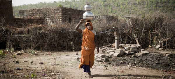 Một người phụ nữ ở vùng nông thôn Ấn Độ đội thùng nước trên đầu. Phụ nữ ở các nước đang phát triển phải mất rất nhiều thời gian để tìm nguồn nước do thiếu cơ sở hạ tầng