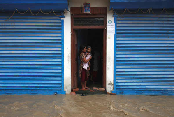 Người phụ nữ bế một đứa trẻ đứng ở cửa nhà trong khu vực bị ngập lụt sau cơn mưa không ngừng ở Bhaktapur, Nepal vào ngày 12/7/2018. Ảnh: Navesh Chitrakar