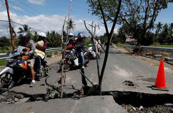 Một gia đình đi xe máy qua vết sạt lở trên đường ở huyện Kayangan sau khi trận động đất tấn công phía Bắc Lombok, Indonesia vào tối 5/8
