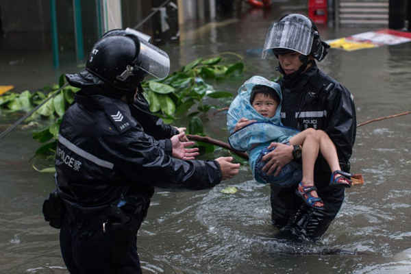 Cảnh sát giải cứu một đứa trẻ từ con đường bị ngập lụt trong siêu bão Mangkhut ở Lei Yue Mun. Ảnh: Jérôme Favre / EPA