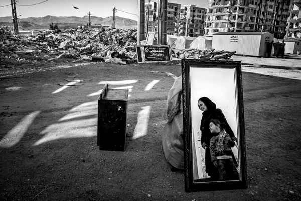 Hình ảnh mang tên “And Life Rises” của tác giả người Iran, Younes Khani Someeh Soflaei – chủ nhân của giải thưởng môi trường xây dựng. Một người phụ nữ và cô con gái nhỏ của cô đứng bên cạnh đồ đạc hư hỏng của họ - những đồ được thu hồi từ đống đổ nát của ngôi nhà của họ ở Sarpol-e Zahab. Khu tòa nhà của dân cư Mehr bị tàn phá sau trận động đất hồi năm 2017 đã làm chết hơn 600 người