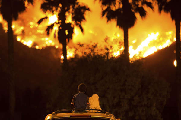 Cậu bé King Bass, 6 tuổi, ngồi và nhìn ngọn lửa có tên gọi Holy bốc cháy từ trên đầu chiếc xe hơi của cha mẹ em trong khi em gái của cậu, Princess, 5 tuổi tựa đầu vào vai anh ở hồ Elsinore, California vào ngày 9/8. Ảnh: Patrick Record / AP