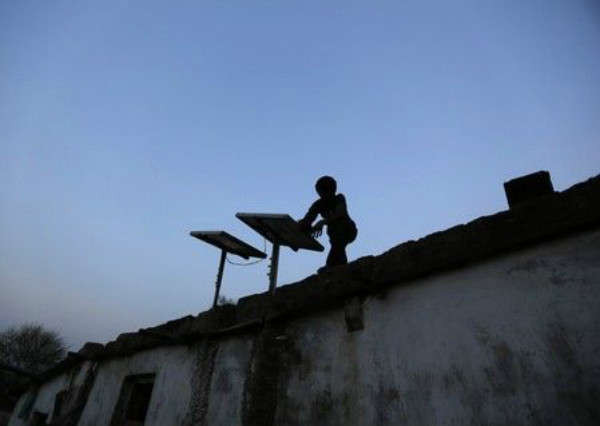 Một cậu bé lau bụi tấm pin mặt trời được lắp đặt trên tầng thượng của ngôi nhà cậu ở ngoại ô thành phố Ahmedabad, bang Gujarat, Ấn Độ